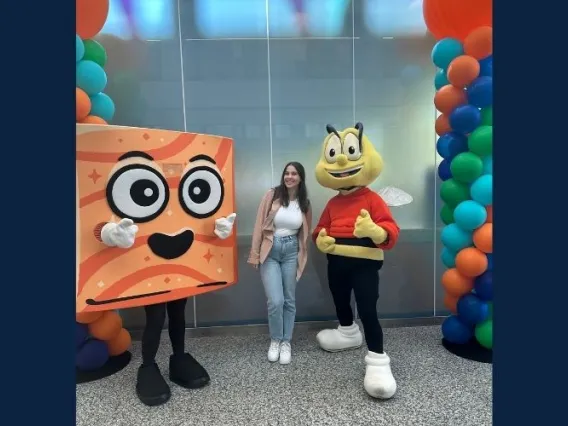 Woman with brown hair smiling next to costumed characters of a bee and animated cereal piece.