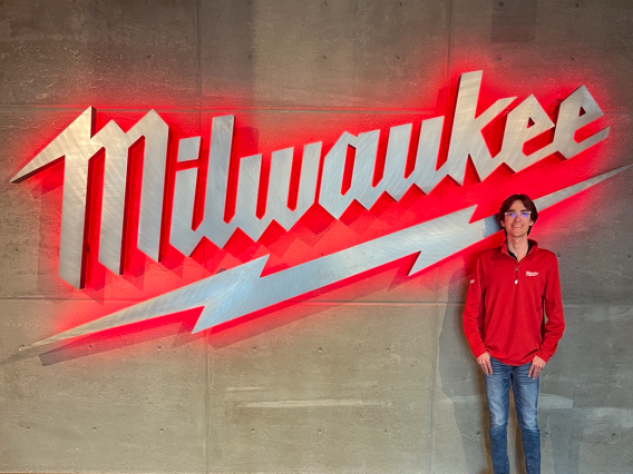 Man in red shirt standing in front of a neon Milwaukee sign.
