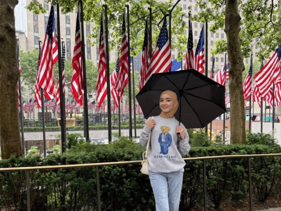 Setora wearing an Eller sweatshirt under an umbrella in front of a row of USA flags. 