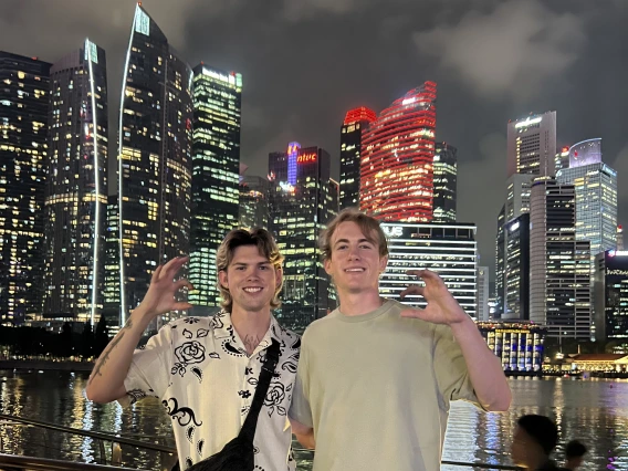 two students in front of Singapore skyline with "Wildcats" hand symbol