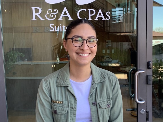 Dulce Tellez standing in front of glass door with R&A CPAs logo.
