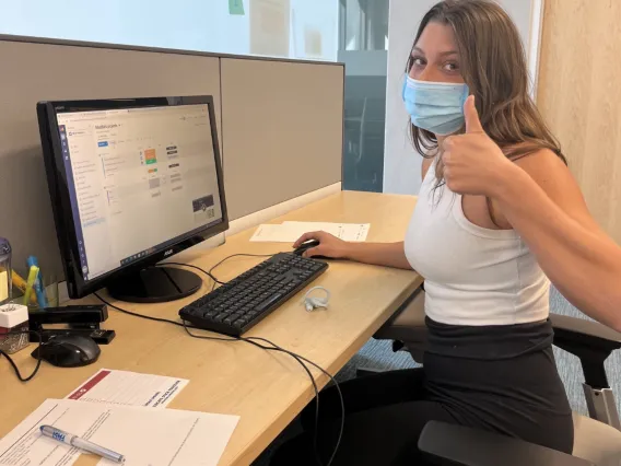 Maddie Zook sitting at her desk showing her computer with a thumbs up.