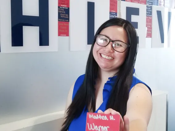 Mattea Hanson holding a name card and standing in front of Eller's achieve wall.