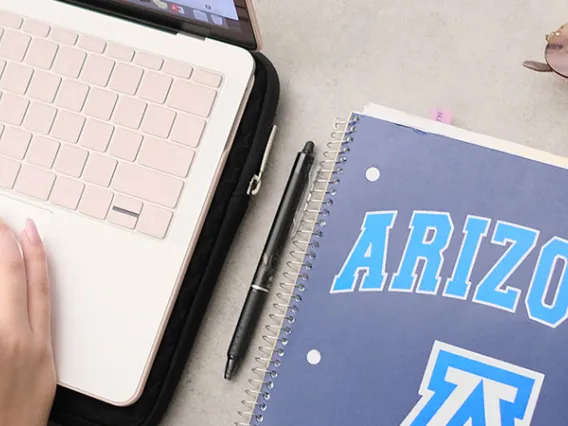 Hand on laptop computer with University of Arizona notebook