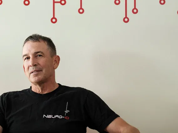 Joe Valacich, in a black t-shirt that says "Neuro-ID," leans back against a white wall with red circle and line decals.