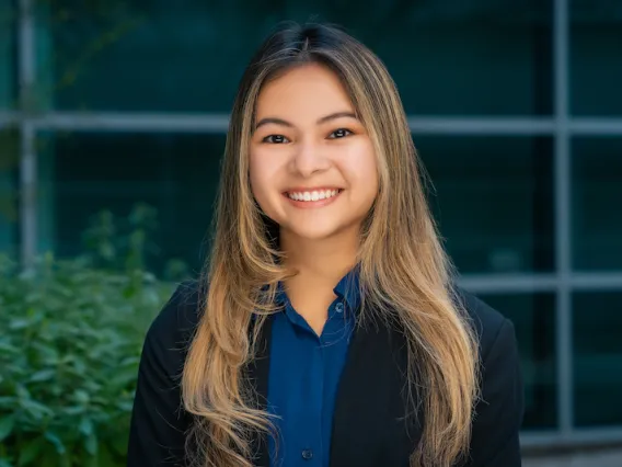 woman with long hair, blue shirt and dark blazer smiling in front of windows