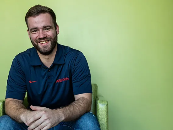 Nick Caswell leans forward in his chair, smiling in front of a green wall. 