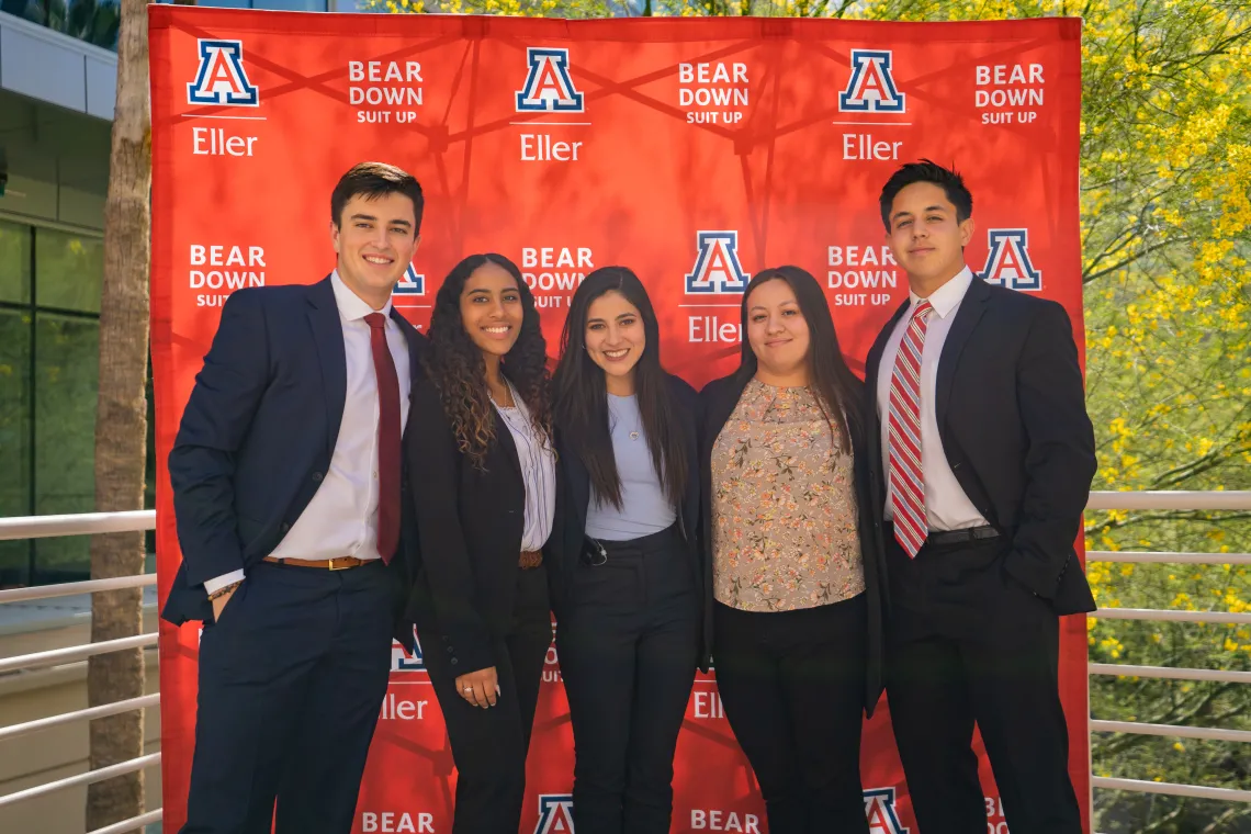 Graduate students smiling in front of Eller banner