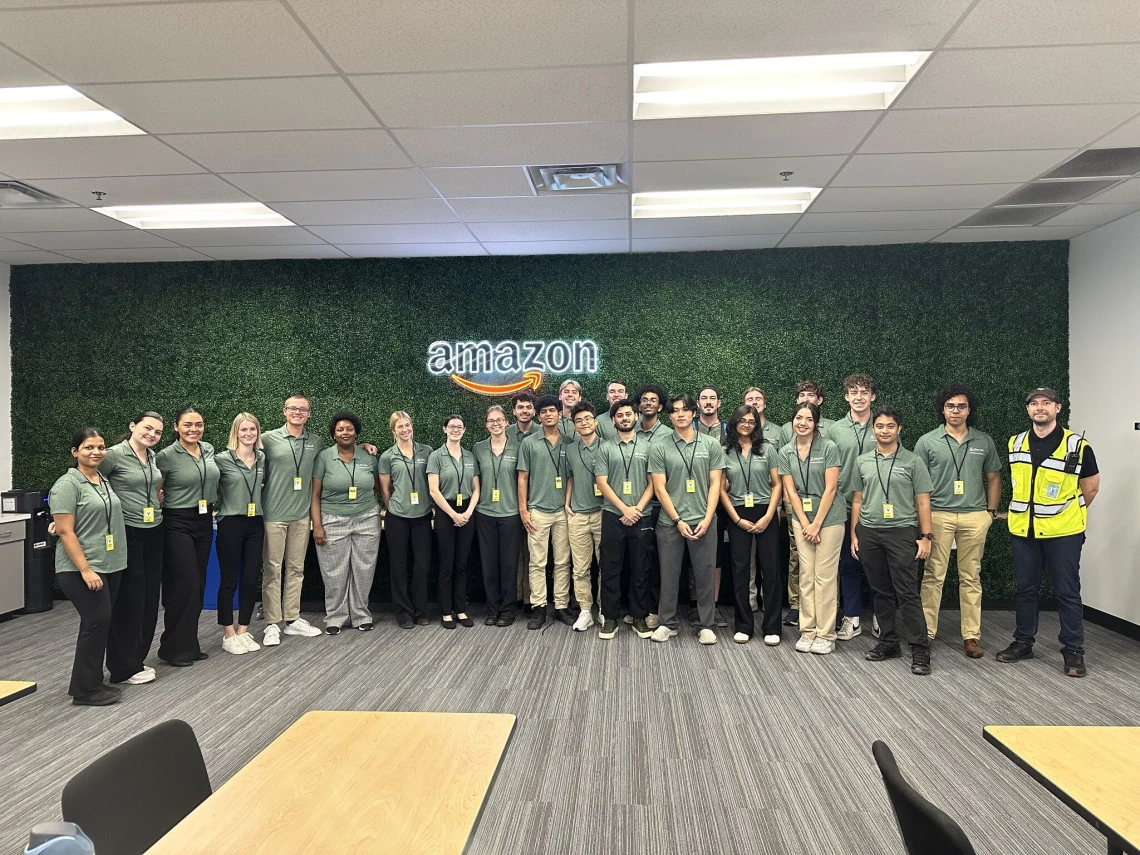 Students wearing green polos and standing in front of an Amazon sign