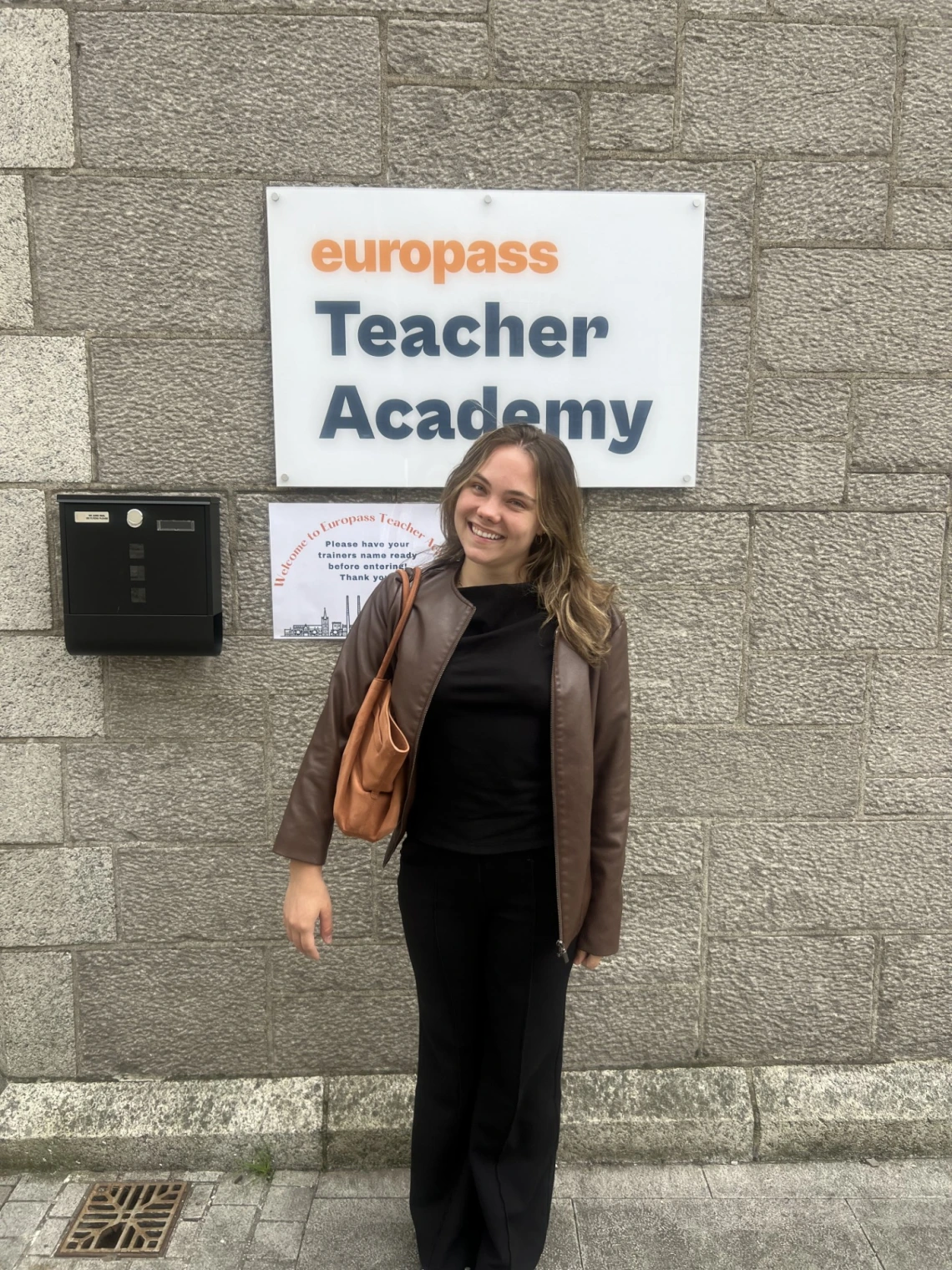 girl standing behind a sign that says "europass teaching academy"
