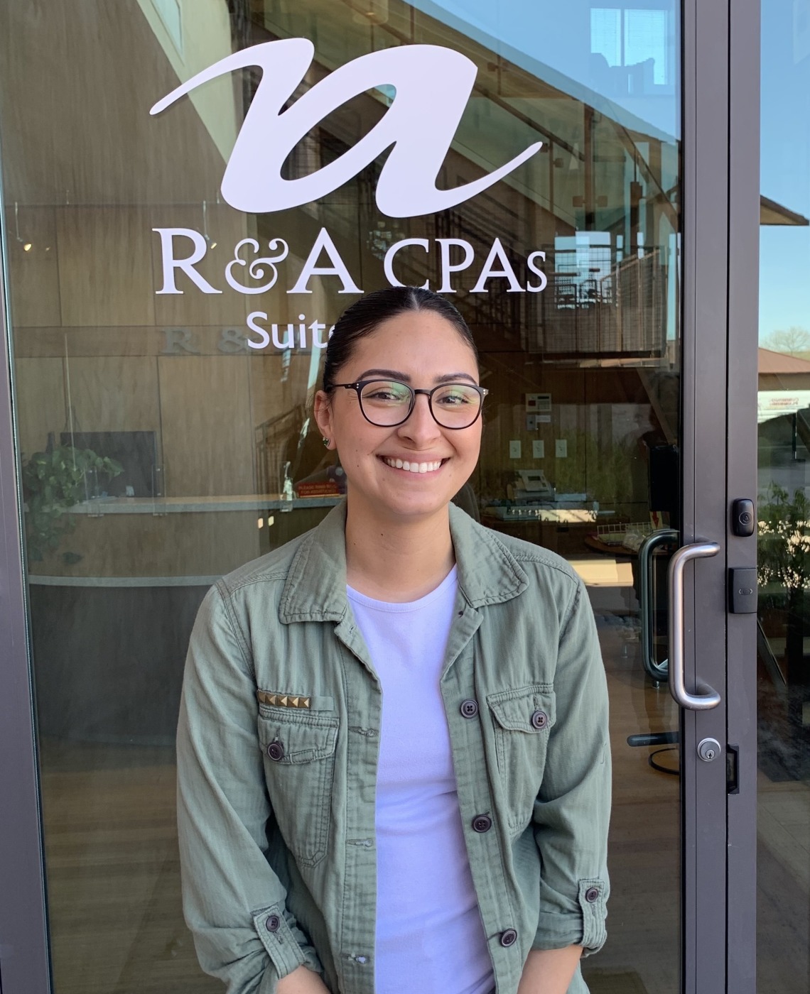 Dulce Tellez standing in front of glass door with R&A CPAs logo.