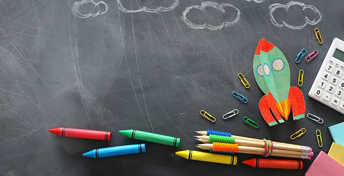 Chalkboard with crayons and clouds drawn in white chalk