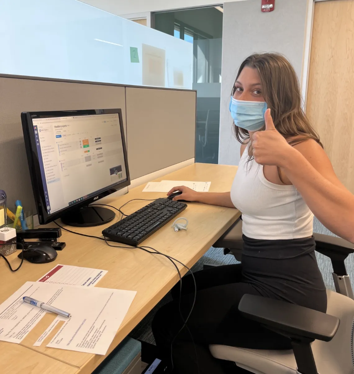 Maddie Zook sitting at her desk showing her computer with a thumbs up.