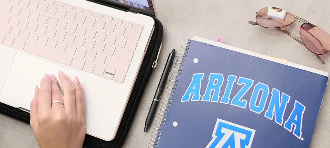 Hand on laptop computer with University of Arizona notebook