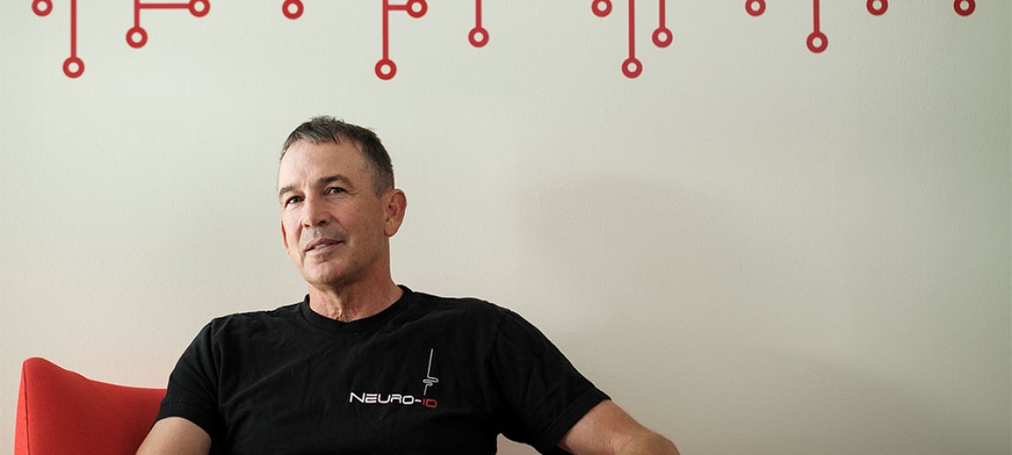 Joe Valacich, in a black t-shirt that says "Neuro-ID," leans back against a white wall with red circle and line decals.