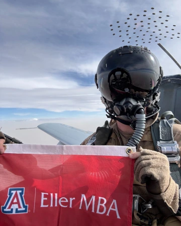 Andrew Huff flying military plane while holding an Eller MBA flag