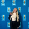 Samantha standing in front of a FIFA back drop. She's displaying the WC ("wildcats") had signal
