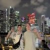 two students in front of Singapore skyline with "Wildcats" hand symbol