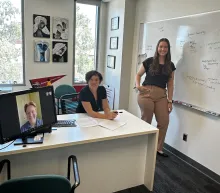 A professor and a student in an office, while another student attends virtually via a computer.