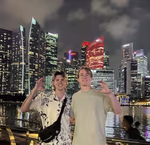 two students in front of Singapore skyline with "Wildcats" hand symbol