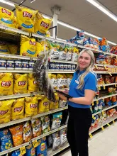 woman in blue shirt and dark pants standing in front of chip aisle in grocery store