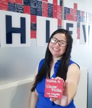 Mattea Hanson holding a name card and standing in front of Eller's achieve wall.