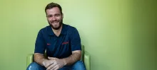 Nick Caswell leans forward in his chair, smiling in front of a green wall. 