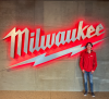 Man in red shirt standing in front of a neon Milwaukee sign.